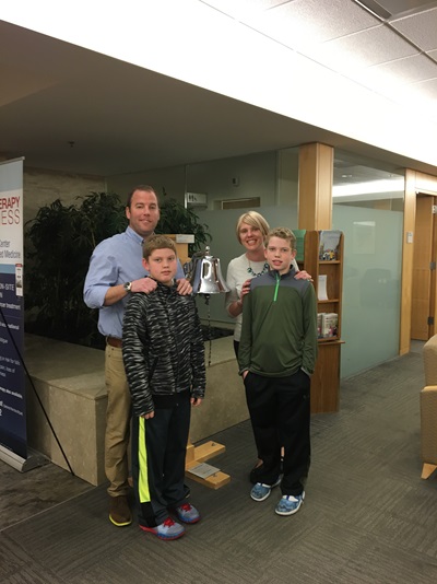 Tracey stands at the Abramson Cancer Center with her husband and two boys next to the bell she just rang to signify the end of her cancer treatment
